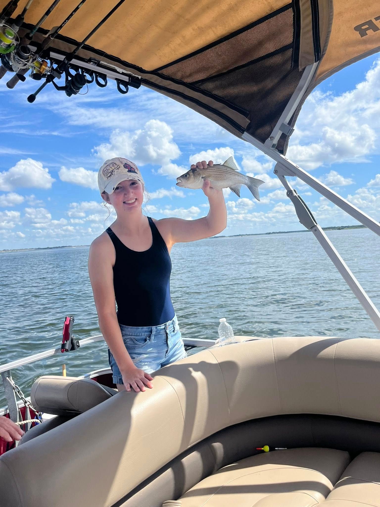 Person on a boat holding up a fish, smiling. Blue sky and water in the background.
