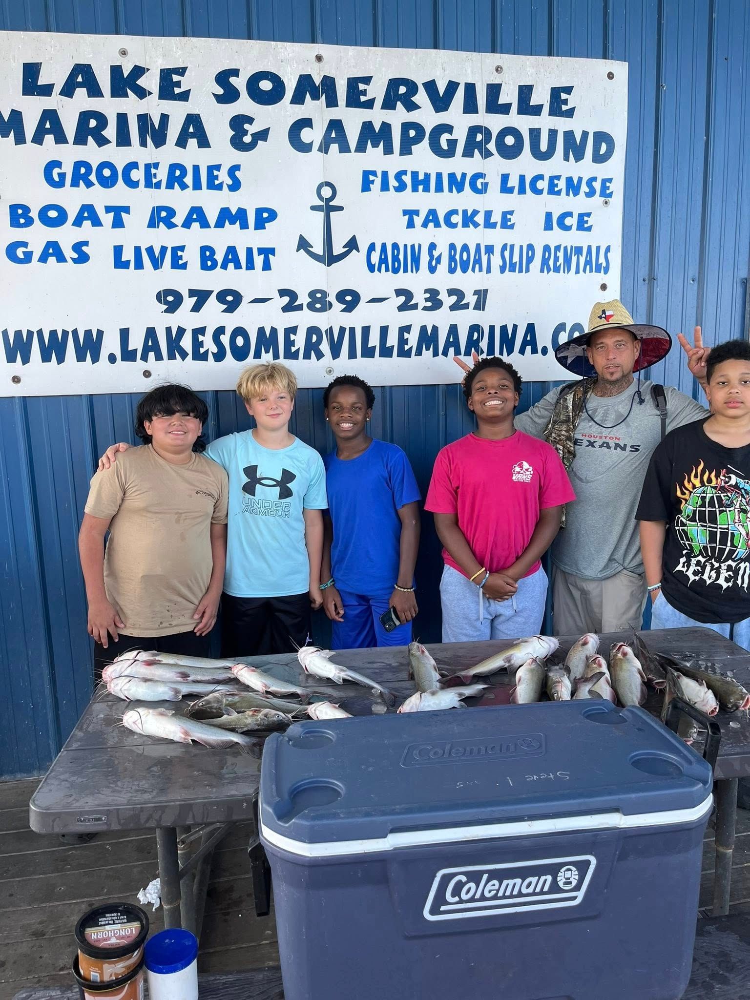People with fish catch posing at a marina. Sign in background advertises services.