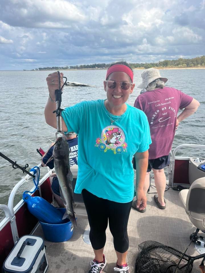 Woman on a boat holding a fish, smiling. Cloudy sky, other people visible.