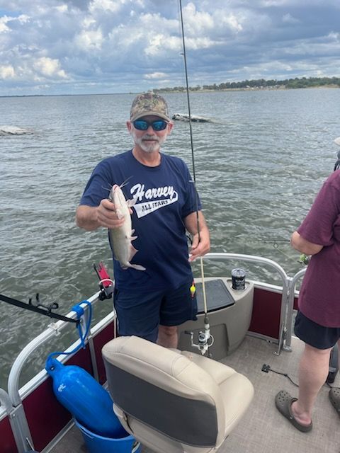 Man on a boat holding a fish, cloudy day, lake in the background.