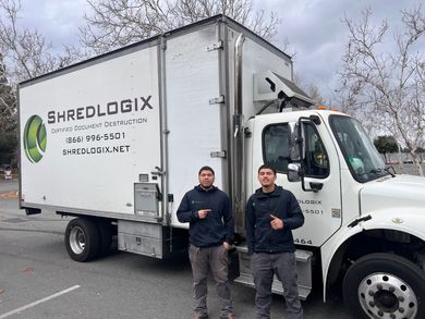 Two men are standing in front of a shredlogix truck.