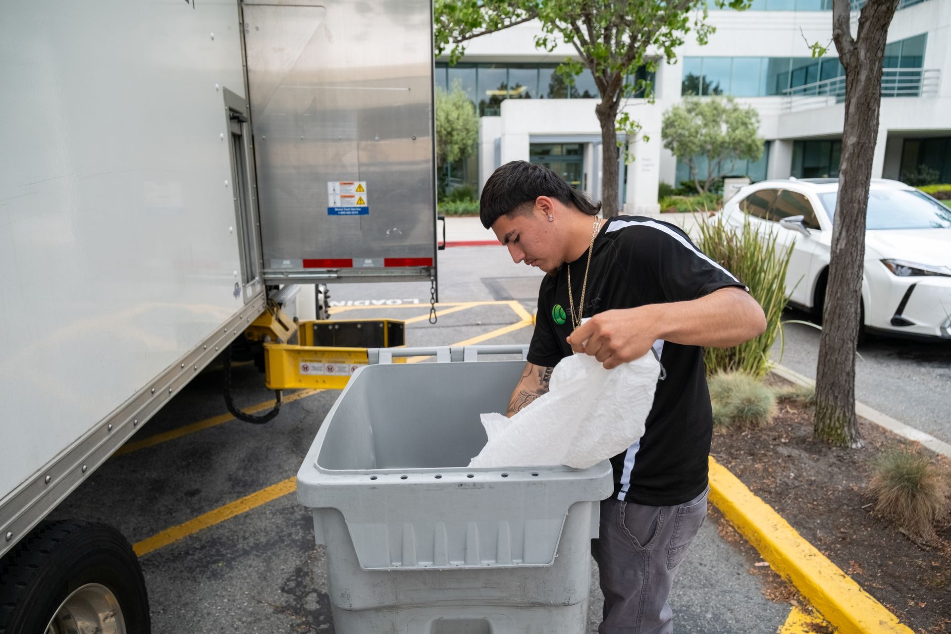 A man is loading a trash can into a truck in a parking lot.