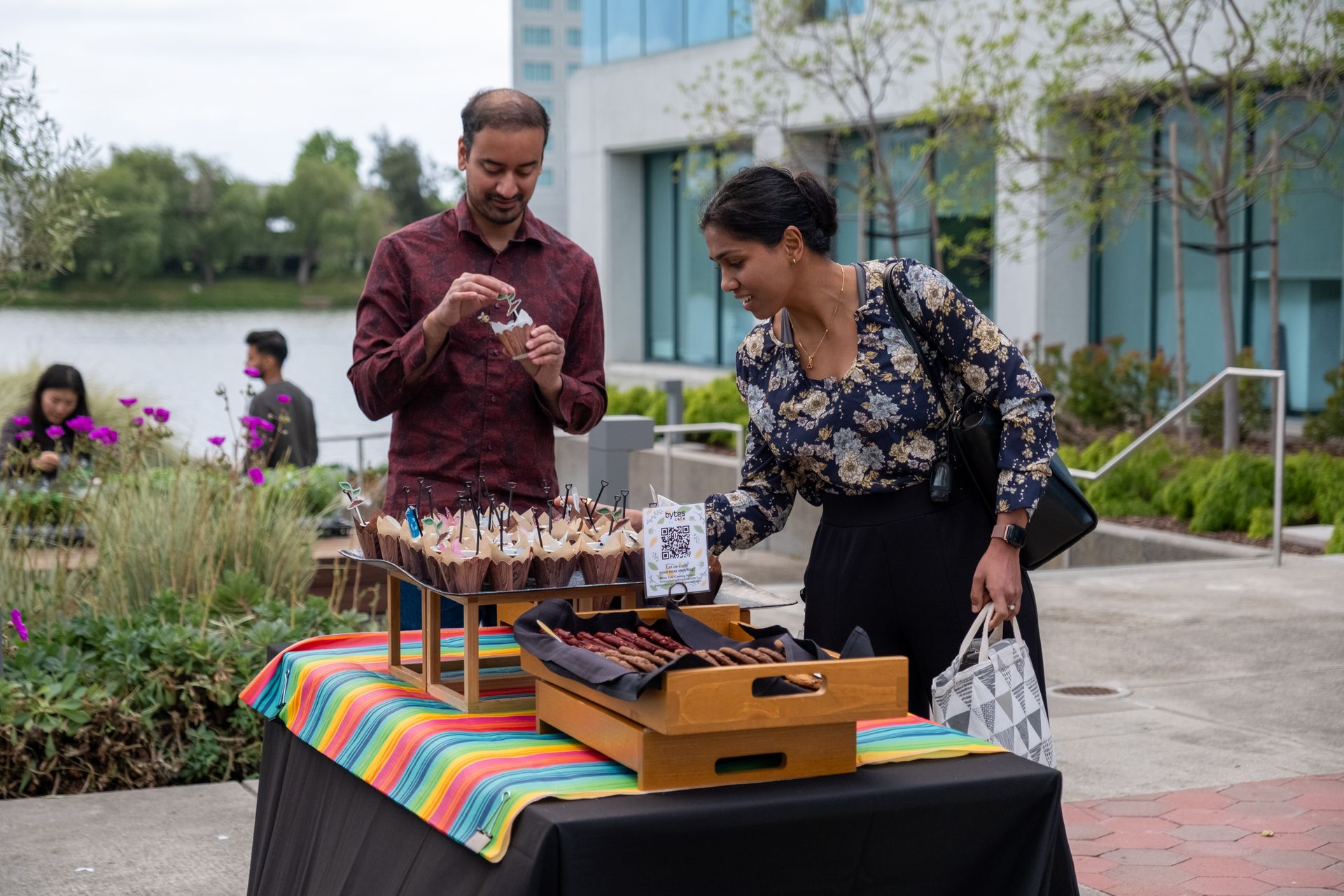 A man and a woman are standing next to a table with cupcakes on it.