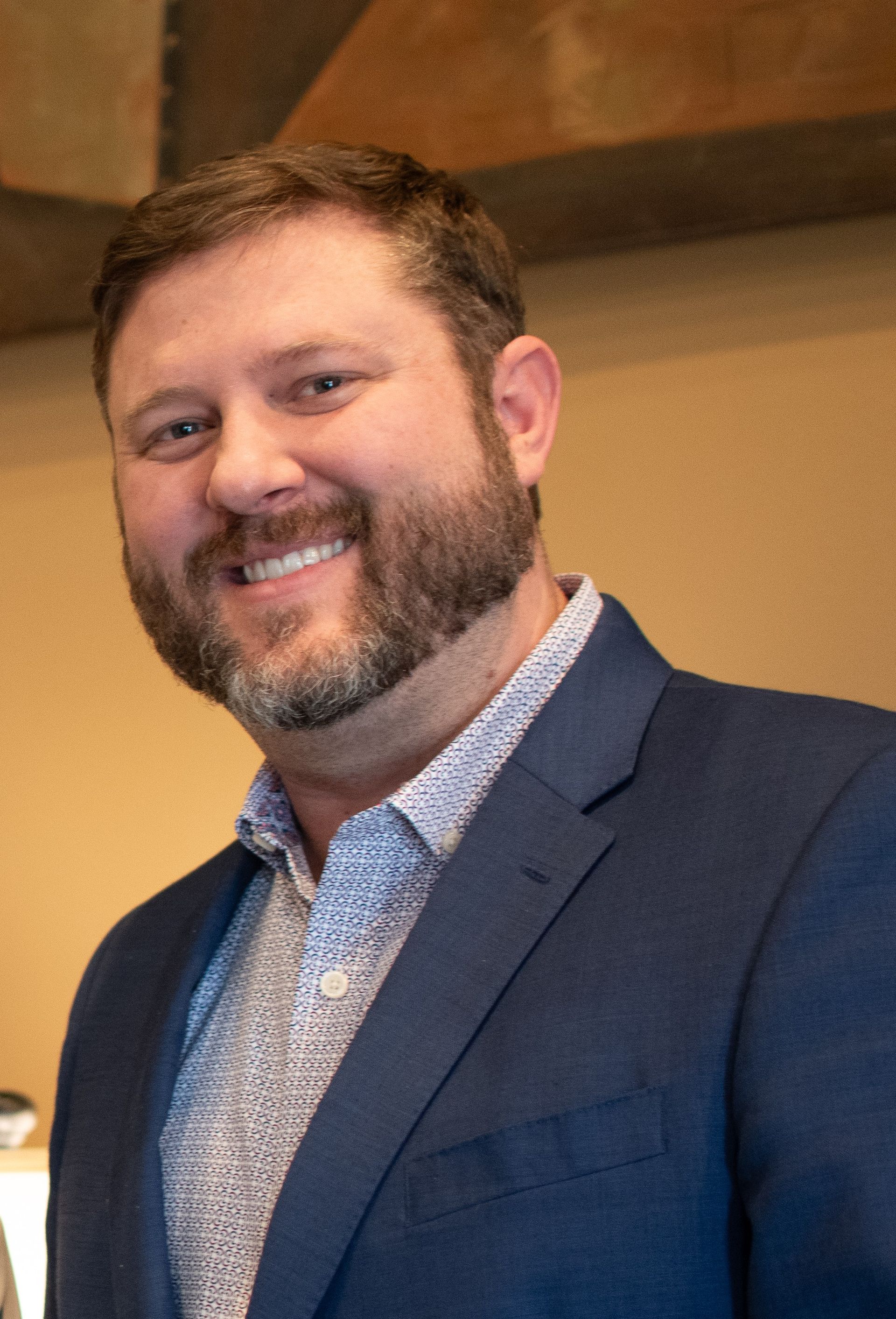 A man with a beard is wearing a blue suit and smiling.