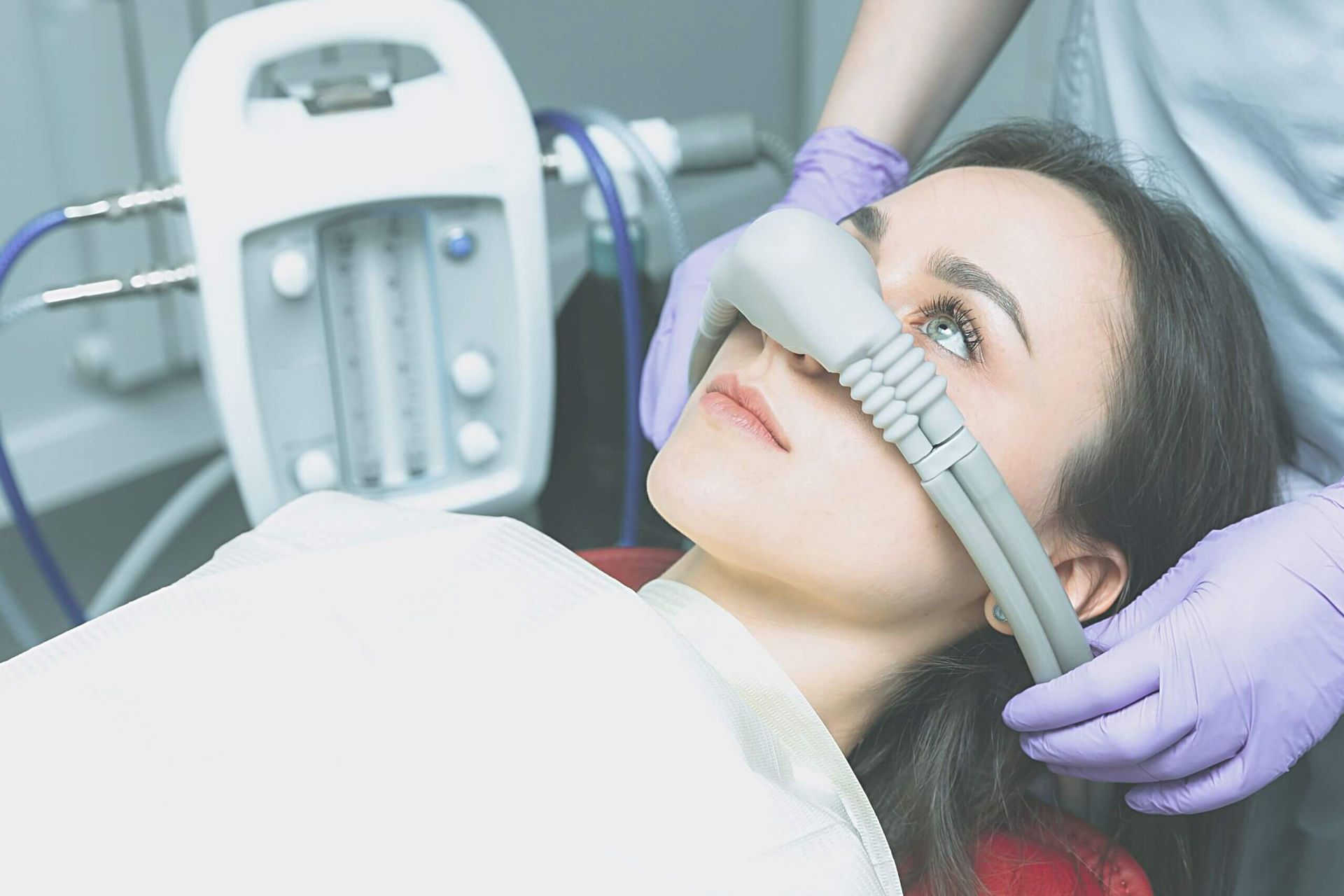 A woman is laying in a dental chair with an oxygen mask on her nose.