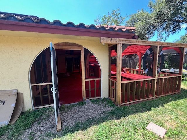 Yellow stucco building with a red-carpeted entryway and a wooden gazebo-like structure to the right