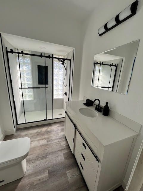 Modern bathroom: white vanity with black fixtures, glass shower, toilet, and light gray floor