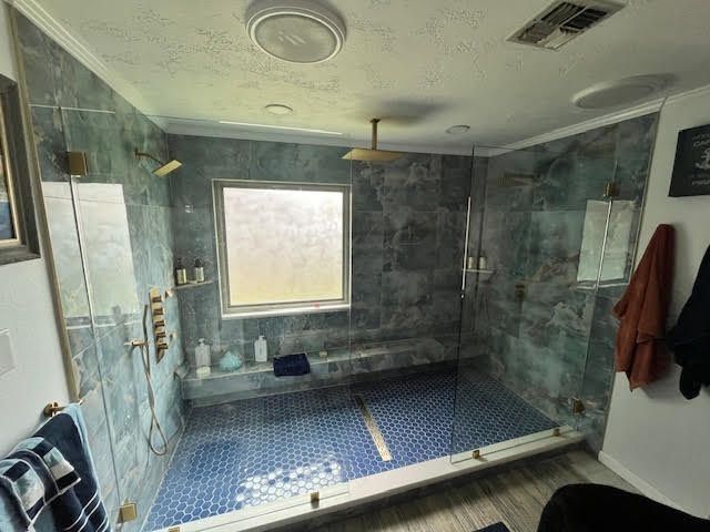 Modern bathroom with blue tile shower, glass doors, and gold fixtures