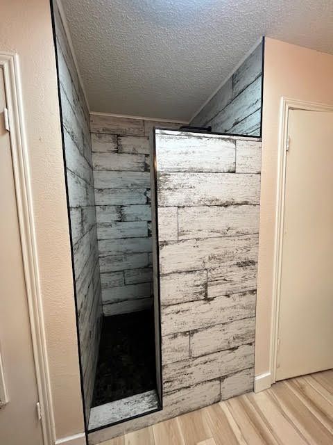 A walk-in shower with white, distressed wood-look panels, black trim, and a dark floor, in a hallway