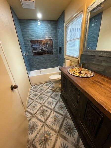Bathroom with blue tile shower, vanity with ornate sink, patterned floor tile