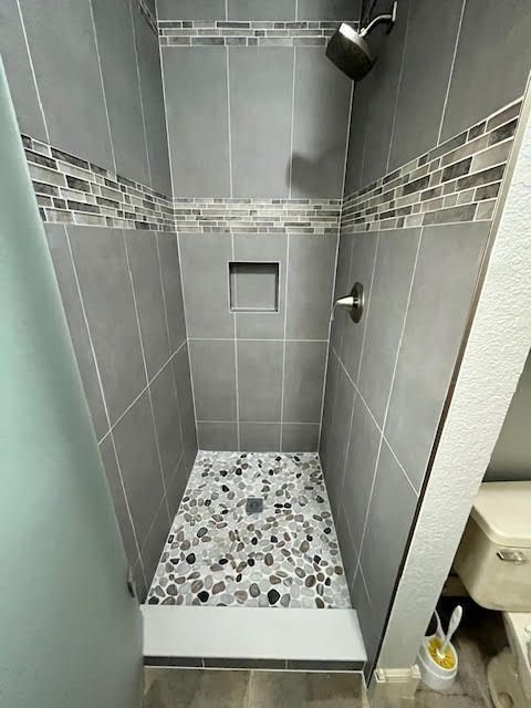 Gray-tiled shower with pebble floor, mosaic accent, and recessed shelf. Showerhead and faucet visible