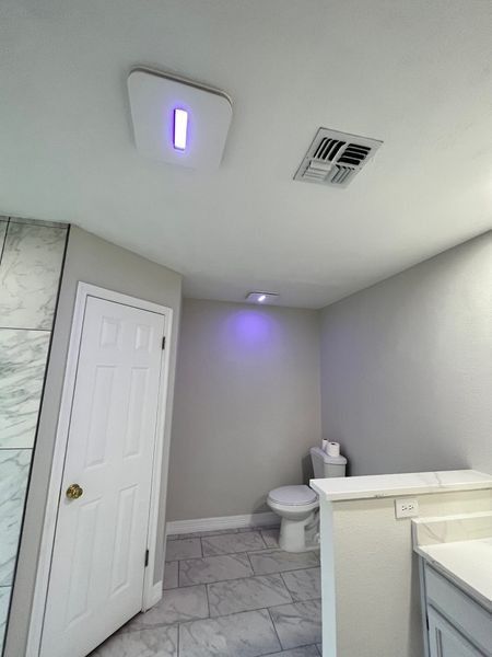Bathroom with toilet, door, and ceiling air purifier emitting purple light