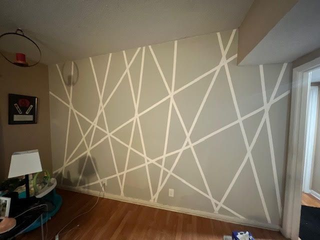 Geometric pattern painted on a gray wall, with white lines, in a room with wooden floors