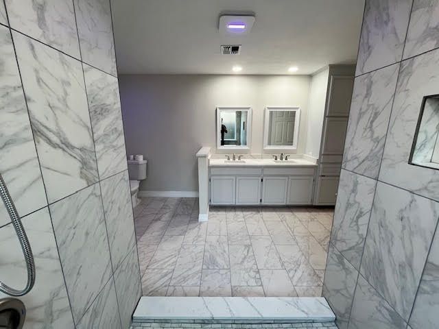 Modern bathroom with marble tile, double sinks, and a toilet visible