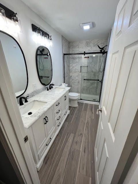 Bathroom with white vanity, oval mirrors, shower, and wood-look floor