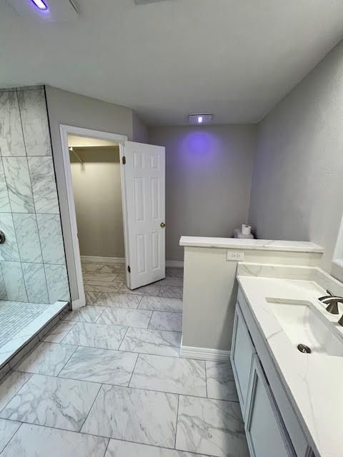 Bathroom with marble tile floor, shower, white vanity, and doorway to a closet