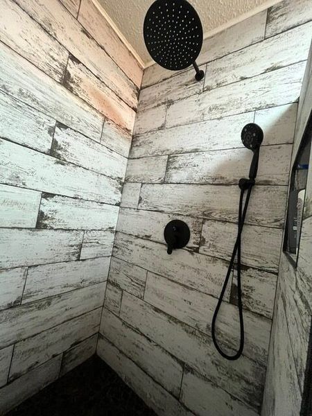 Shower with white-washed wood-look tile and black fixtures, including a rain shower head and handheld