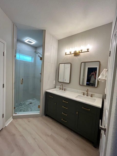 Bathroom with green vanity, two mirrors, a glass shower, and light wood-look flooring