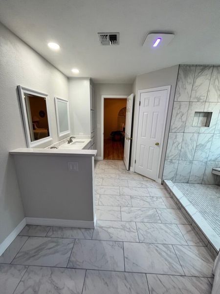 Bathroom with gray walls, tile floor, double vanity, and shower