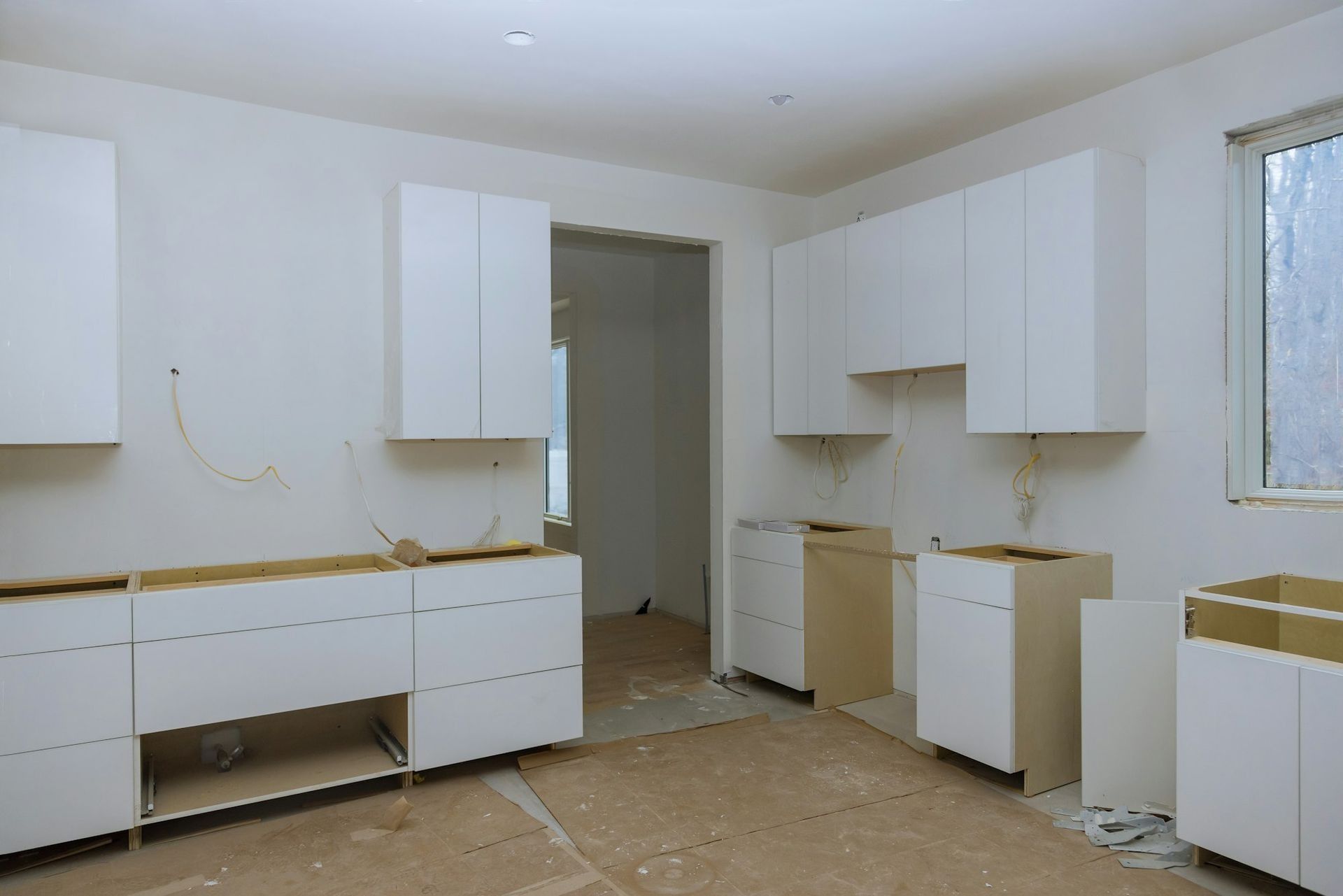 Kitchen renovation in progress: white cabinets installed, unfinished walls and floor