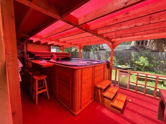 Hot tub under red-tinted wooden canopy on a red deck with steps