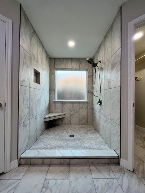 Bathroom shower with marble-look tile, bench, and frosted window