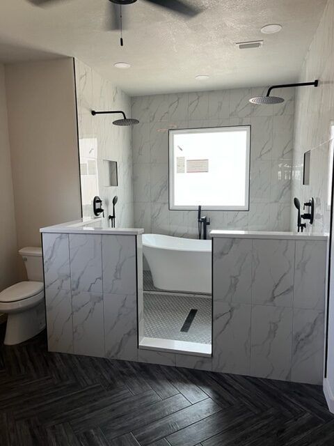 Spacious bathroom with a tub and two showers, white marble walls, dark wood floors