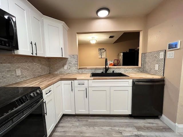 White kitchen with black appliances, a window to another room, and wooden countertops