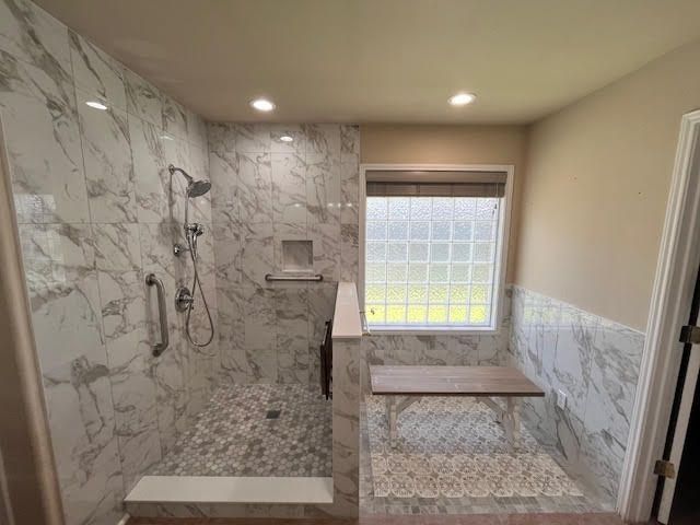 Modern bathroom with marble tile shower, pebble floor, bench, and glass block window