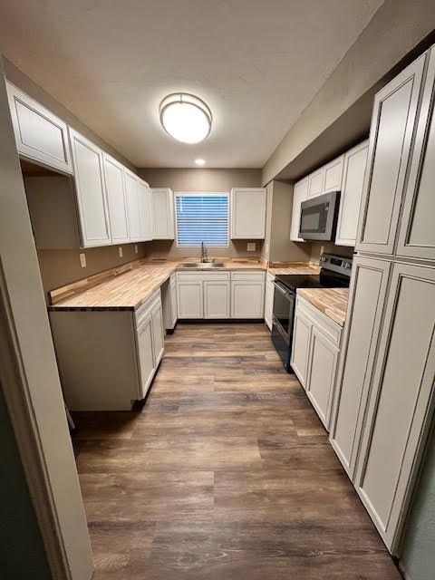 U-shaped kitchen with light wood-look countertops, white cabinets, and dark appliances