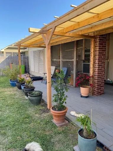 A backyard deck with a pergola, potted plants, and a screened porch