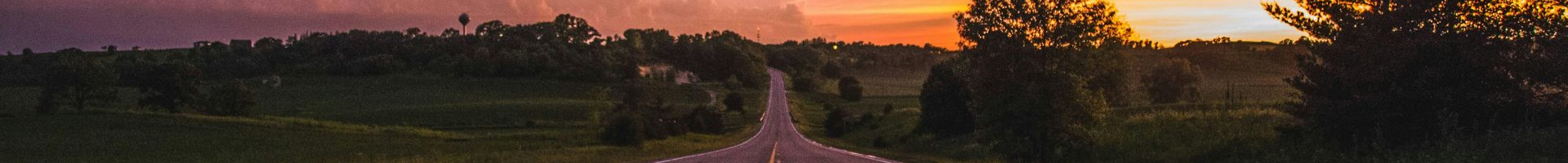Sunset over a road, silhouetted trees, and a dusky sky.