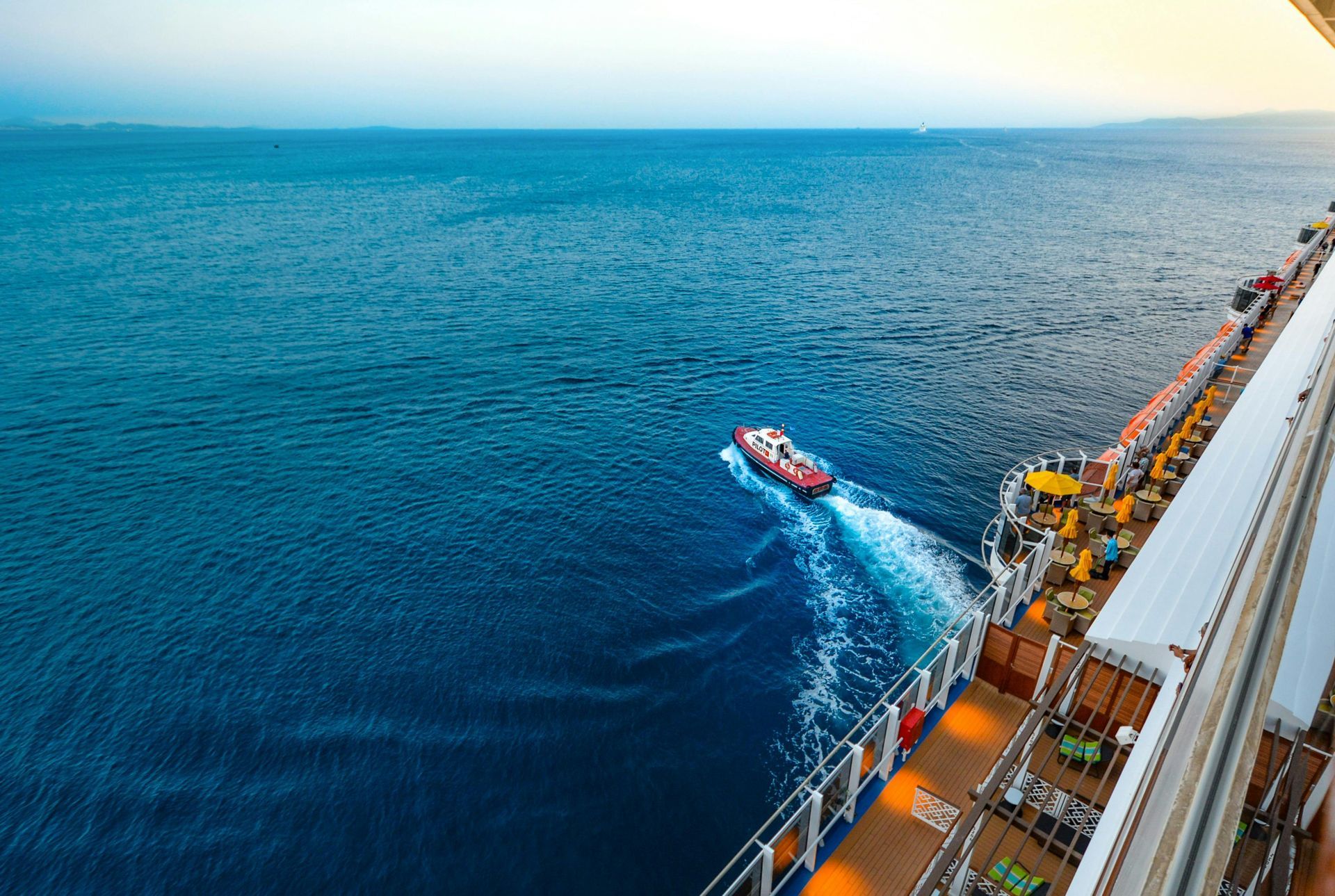 Ocean view from a ship's deck, with a small boat leaving a foamy wake in the blue sea.