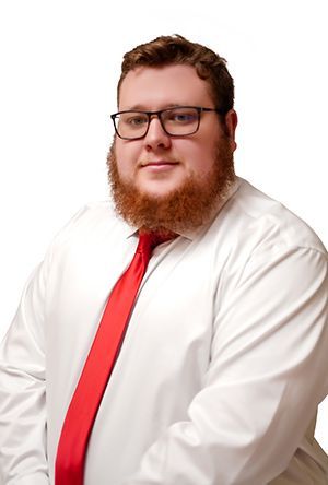 Man with glasses, red tie, and red beard wearing a white dress shirt, smiling.