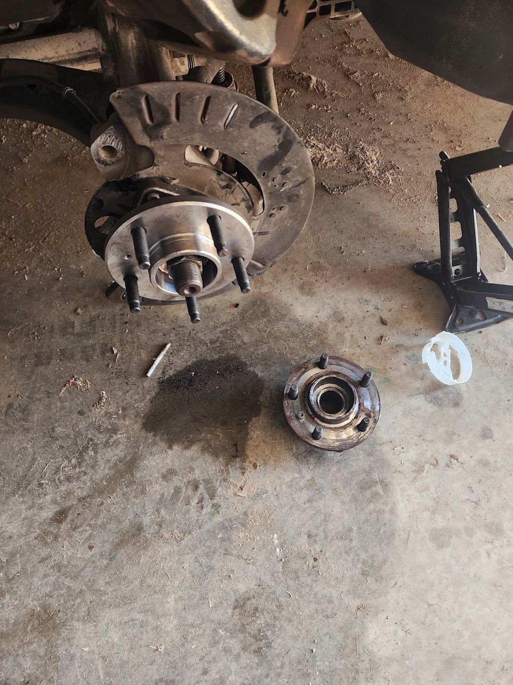 Car wheel hub removed, axle exposed. Disc brake, lug studs, and a jack stand visible. | TST Mechanic Services