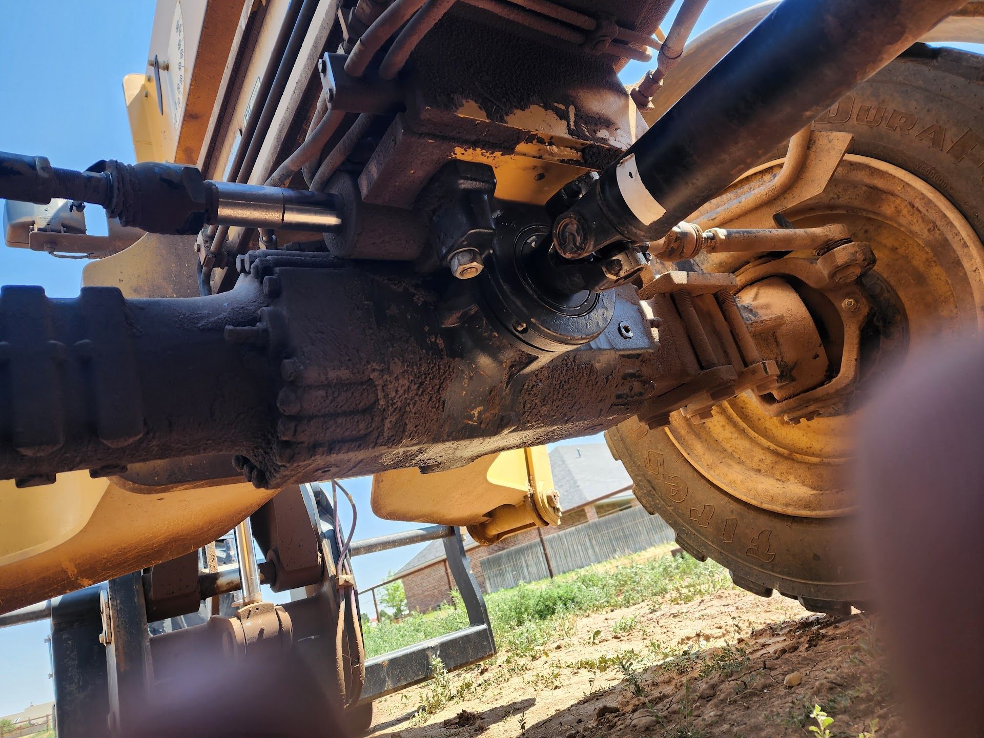 Yellow tractor's undercarriage, covered in oil, showing axle and connecting components. | TST Mechanic Services