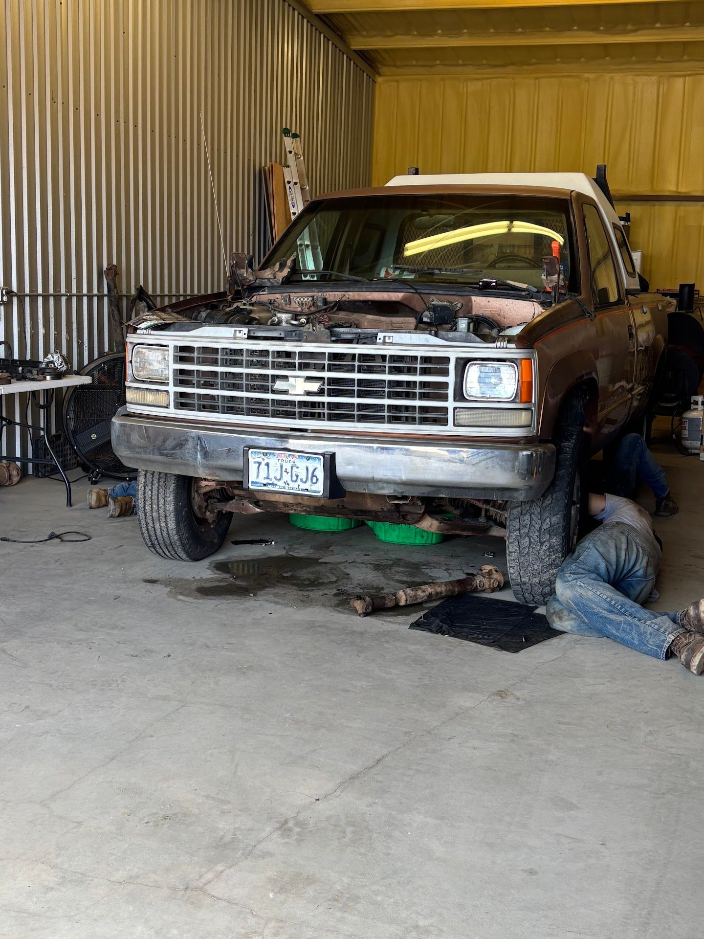 Brown Chevy pickup truck being worked on in a garage; a mechanic lies under the truck. | TST Mechanic Services