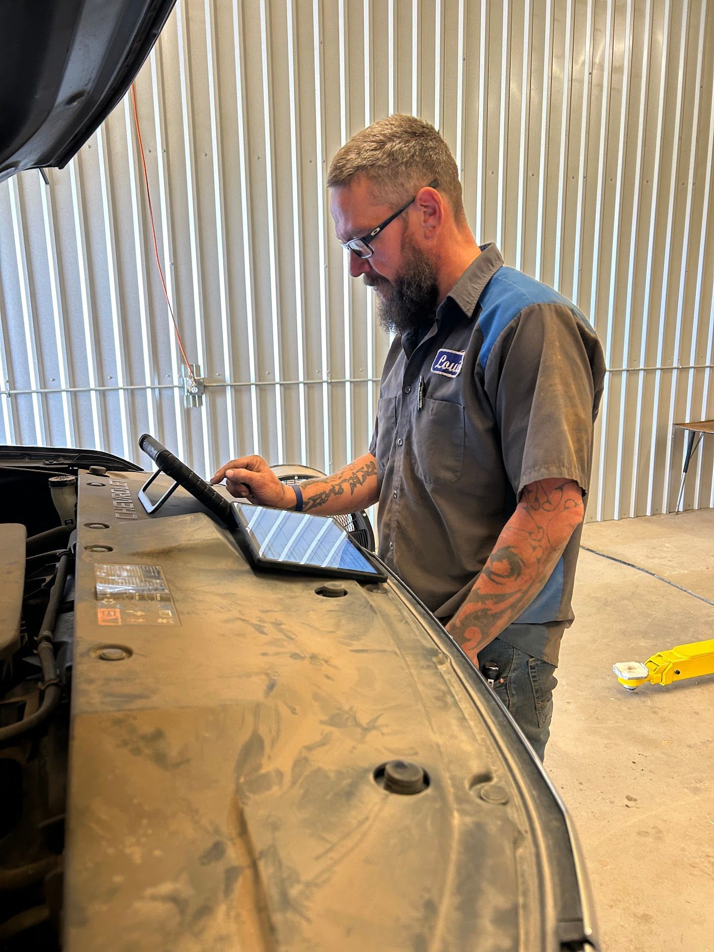Mechanic using a tablet under the hood of a car in a garage. | TST Mechanic Services
