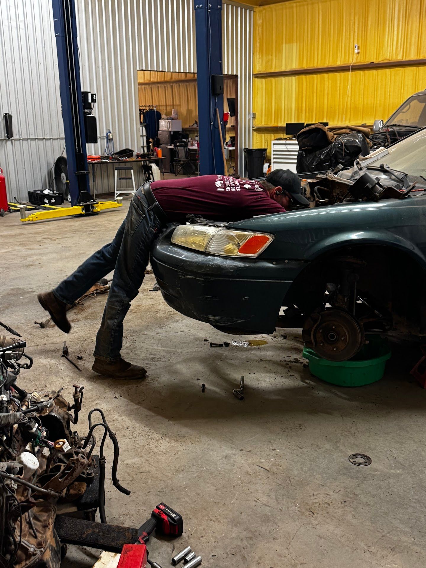 Mechanic working on a teal car in a garage, leaning inside the hood. Tools and car parts are visible. | TST Mechanic Services