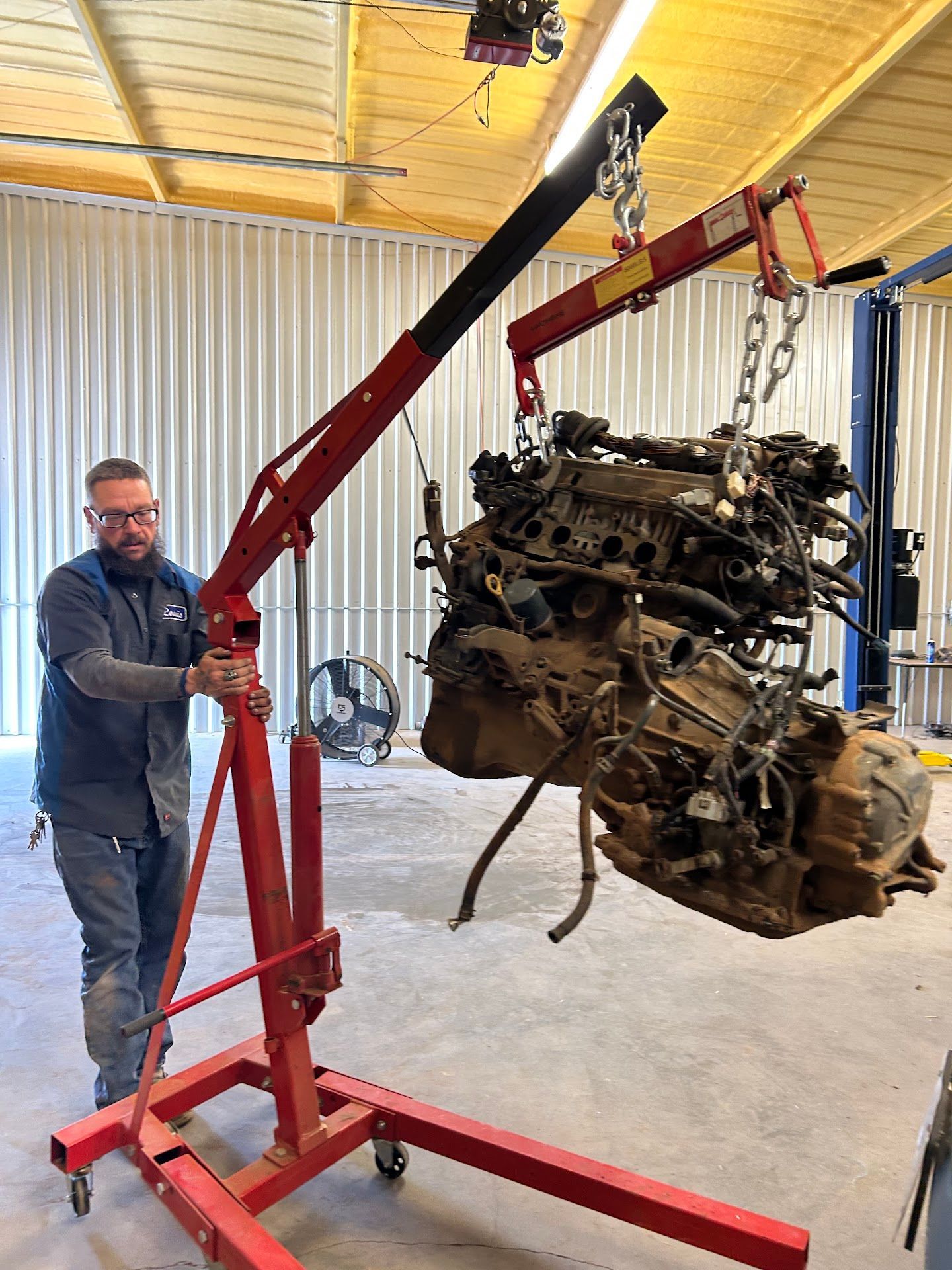 Mechanic using a red engine hoist to lift a dirty engine in a garage. | TST Mechanic Services