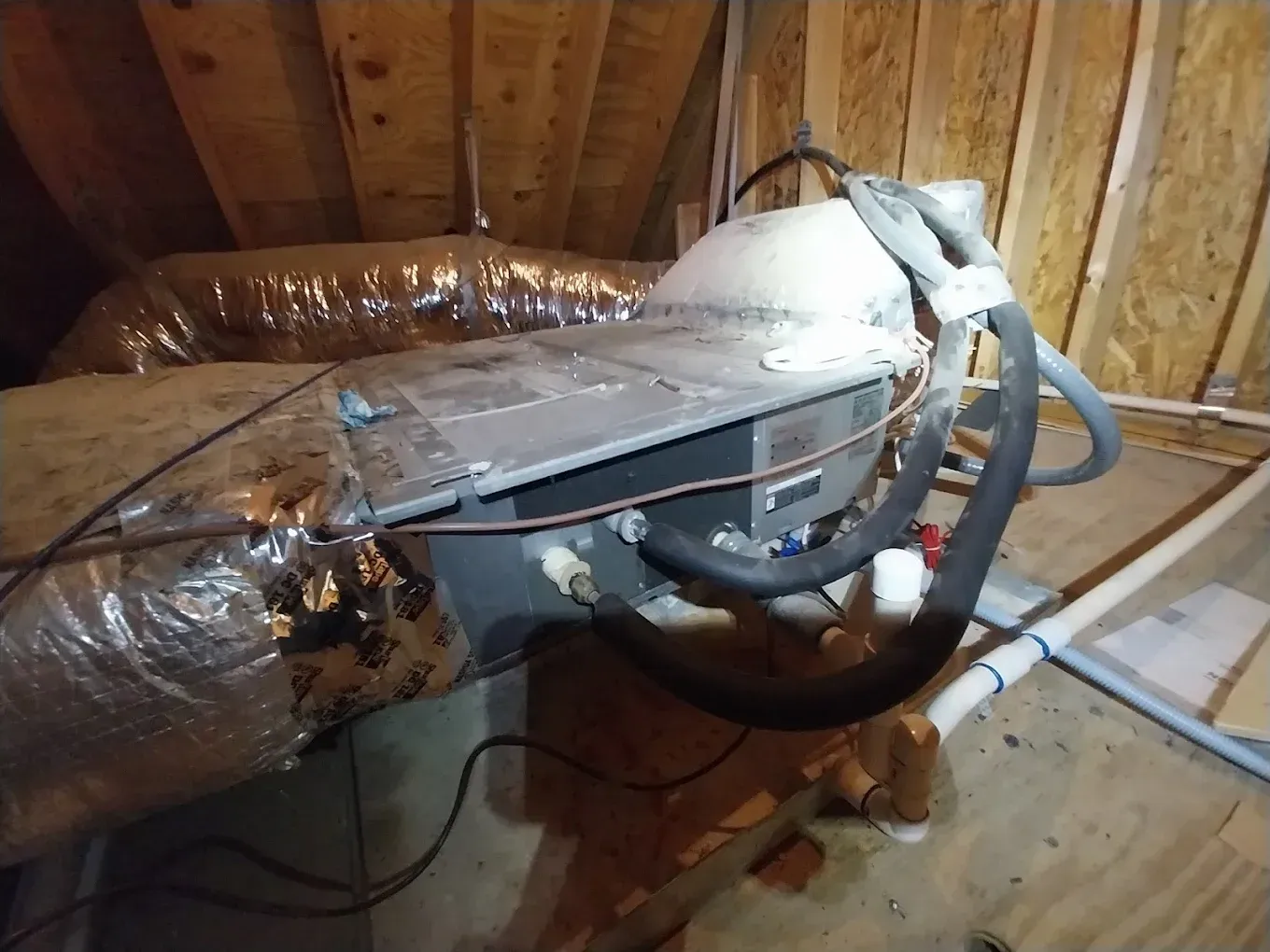 HVAC unit in an attic, with ductwork and pipes, wood beams in the background.