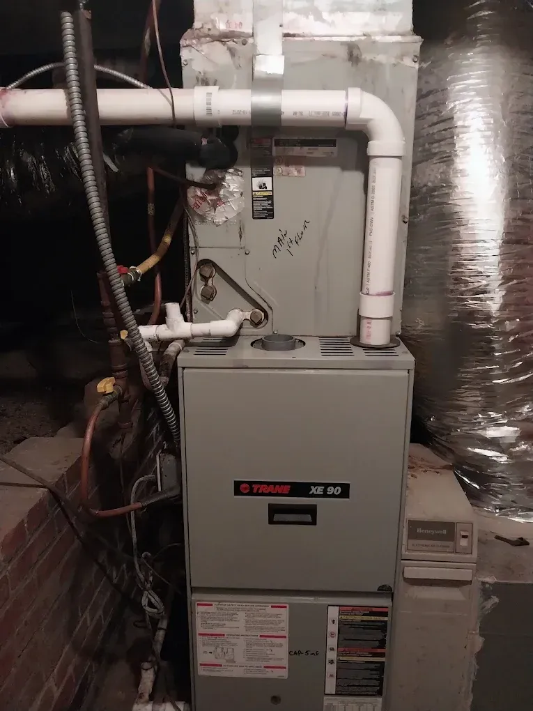 Gray furnace with white PVC pipes in a utility room.