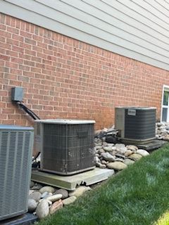 Three air conditioning units along a brick building. Rocks and grass are in front.
