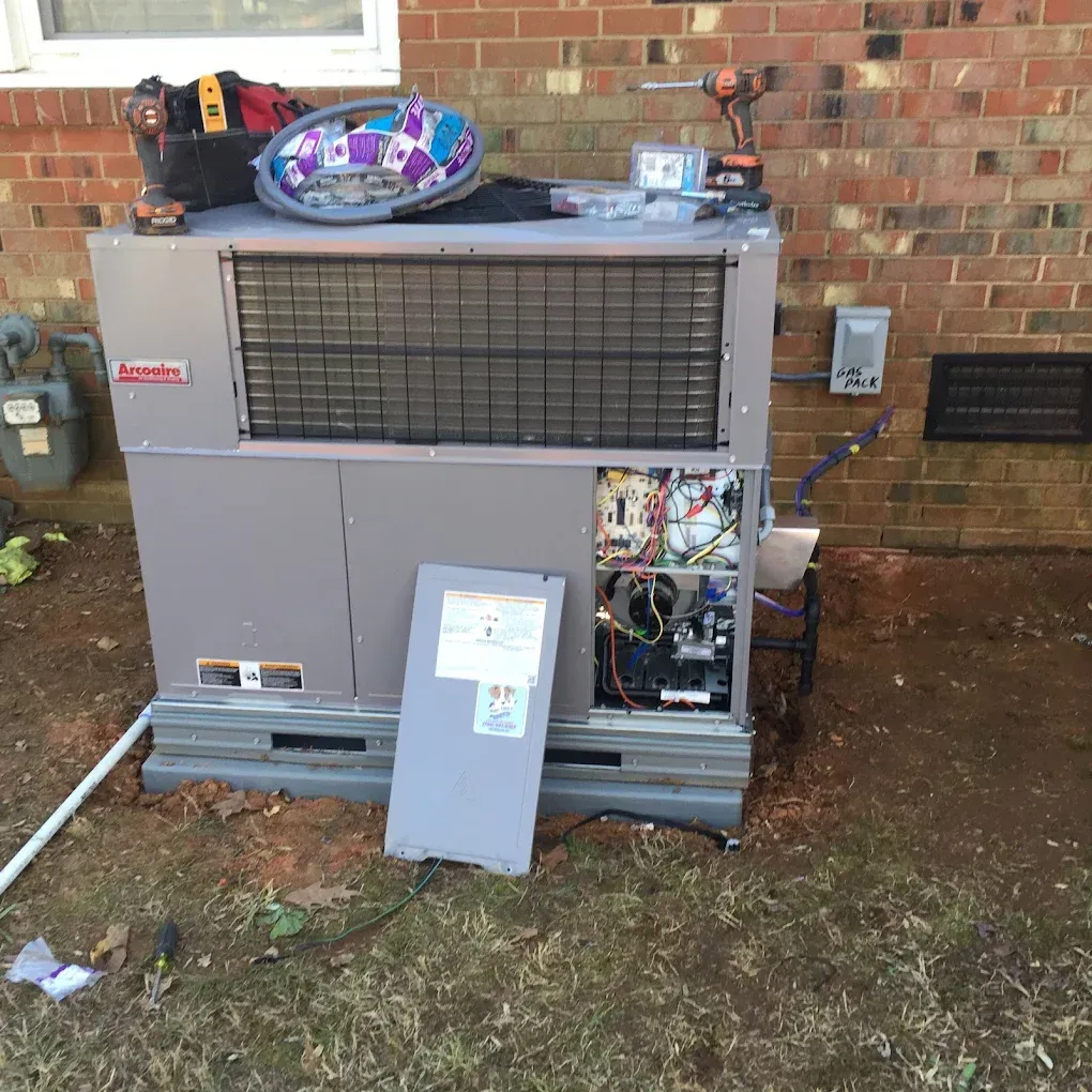 HVAC unit with open panel, tools on top, outdoors near a brick wall.