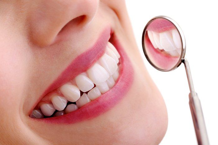 Smiling person with bright white teeth, dental mirror reflects teeth, pink lipstick.
