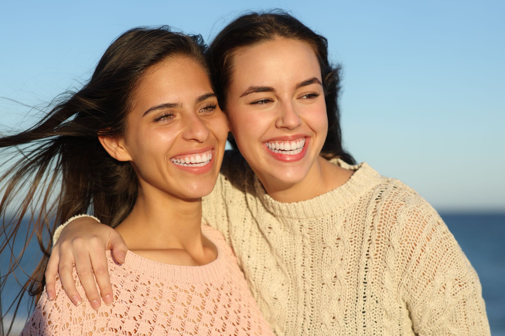 Two people smiling outdoors in cozy sweaters.