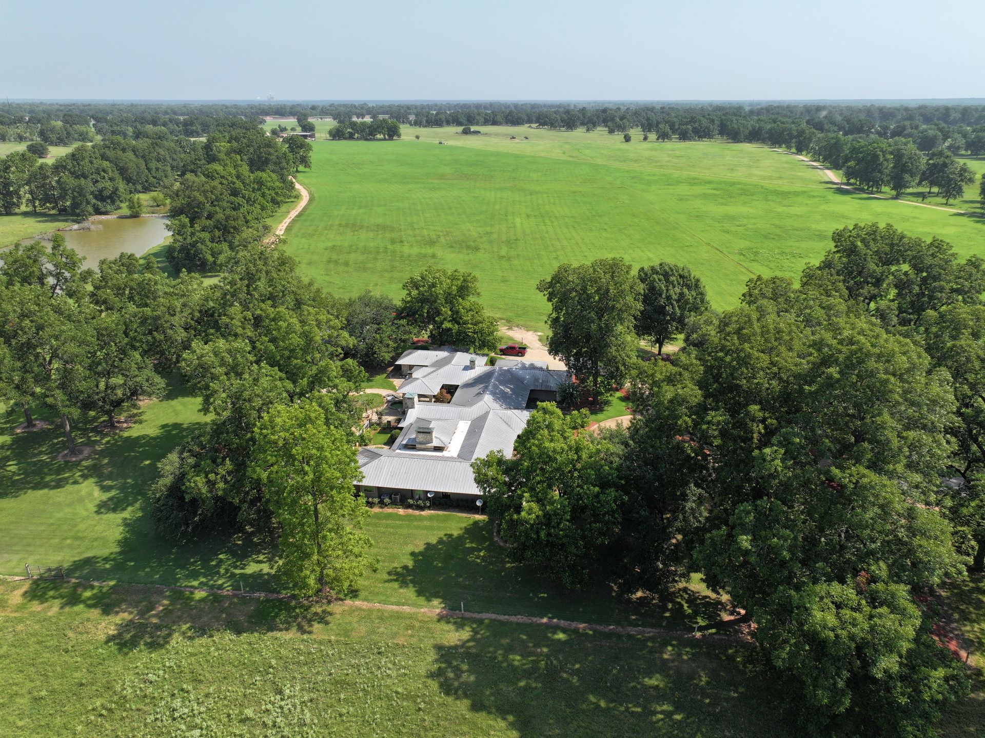 An aerial view of a house in the middle of a lush green field surrounded by trees.