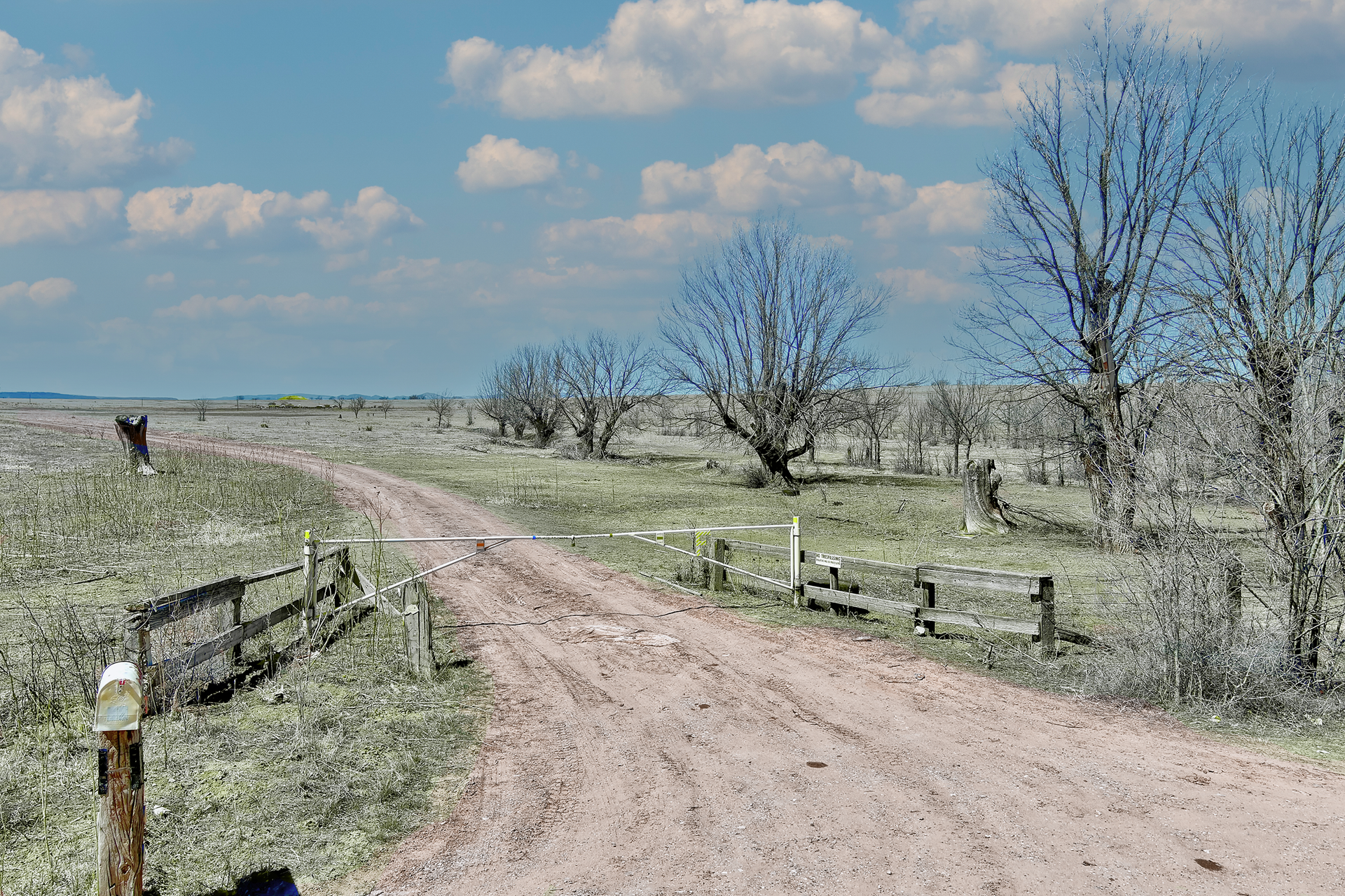 A dirt road going through a grassy field with a fence.