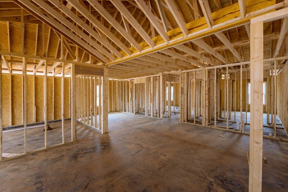 Interior of a house under construction; wooden frame, concrete floor, empty room, natural light.