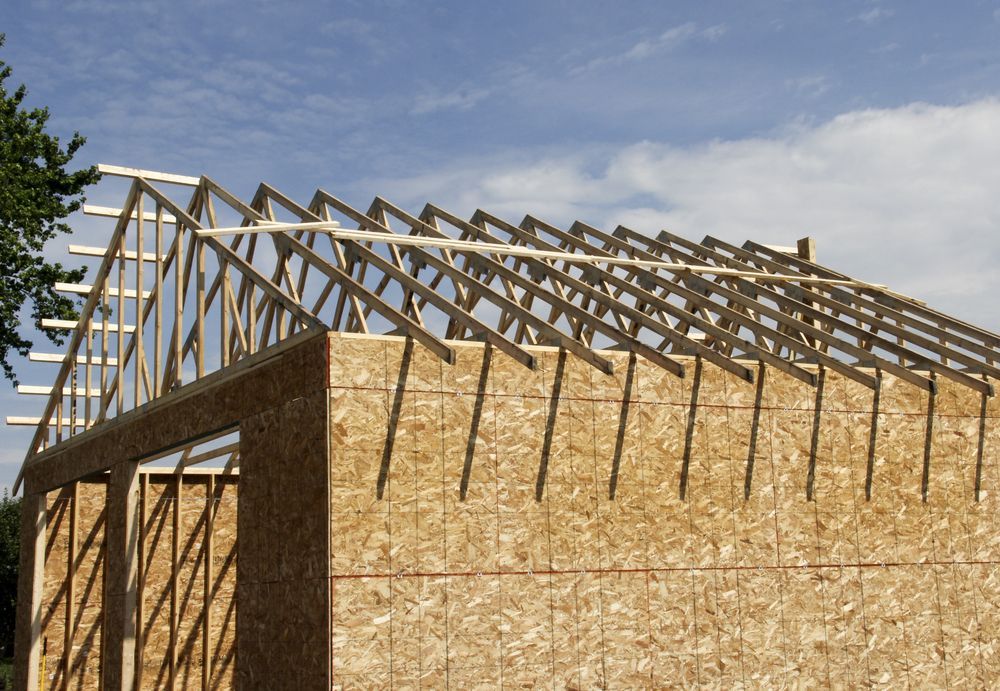Wood frame building under construction, rafters in place on the roof, blue sky backdrop.